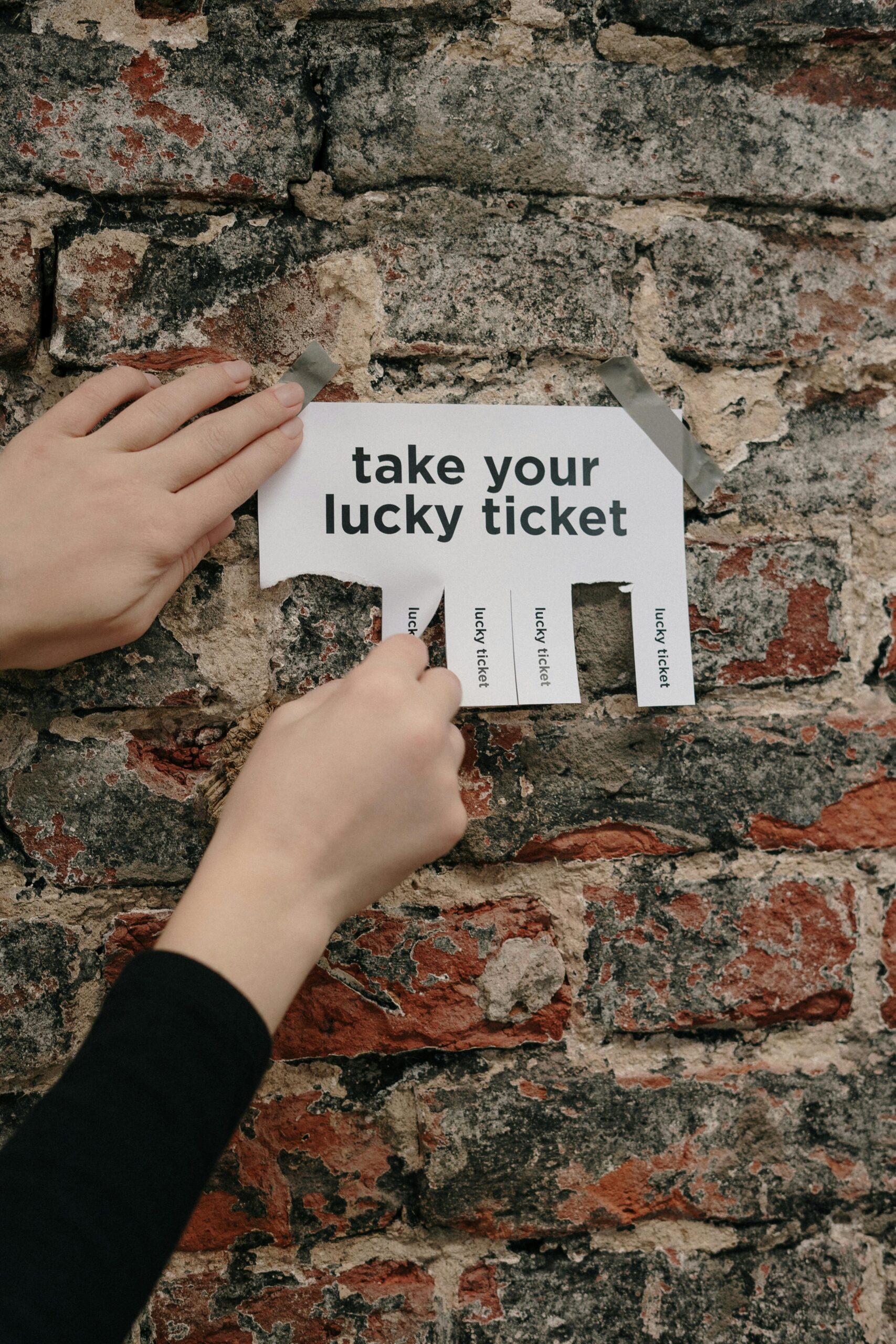 Close-up of hands pulling a lucky ticket from paper on a rustic brick wall.